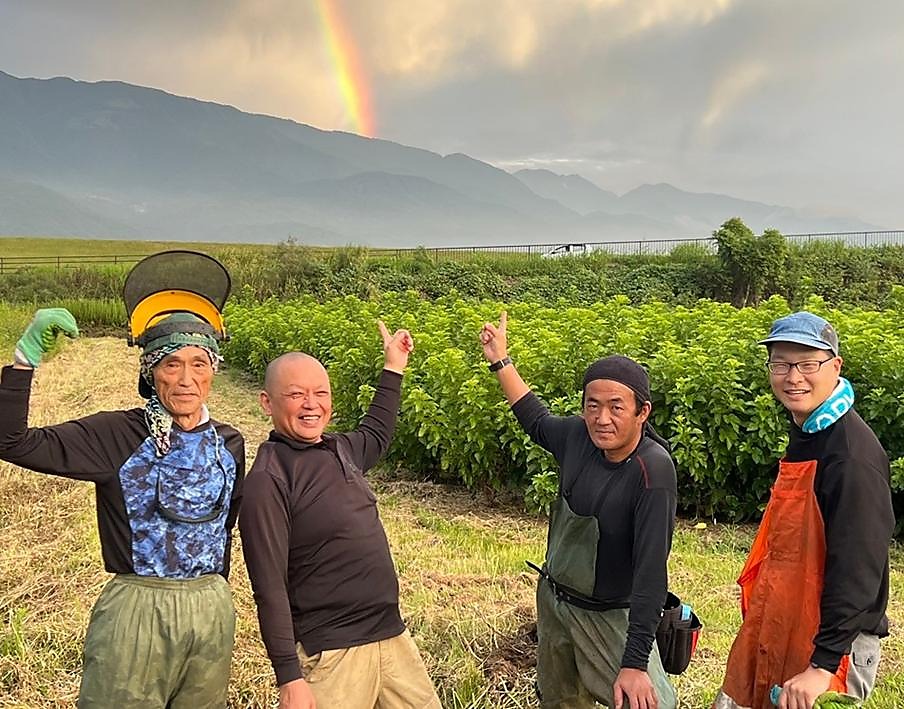 Kuwanosato farming team celebrating in the mulberry fields with a rainbow over the mountains